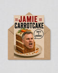 May include: A novelty greeting card with the words "JAMIE CARROTCAKE" in red and black. The image shows a man's face in a slice of carrot cake, with a speech bubble saying "THAT'S A DISGRACE."