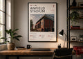 May include: A framed poster of Anfield Stadium, home of Liverpool Football Club. The poster features a photograph of the stadium's exterior, with the words "ANFIELD STADIUM" at the top. The poster is displayed on a wooden desk with a black lamp and a potted plant.