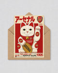 May include: A greeting card with a white lucky cat design in an Arsenal jersey, with red accents and Japanese text. The card features the Arsenal logo and a gold oval with "ARSENAL". The card is inside a brown envelope. The text includes the year 1995.