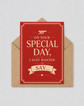May include: A red greeting card with the text "ON YOUR SPECIAL DAY, I JUST WANTED TO SAY..." in a cream-colored font. The card is inside a brown envelope. The card has a decorative border and a small cannon icon.