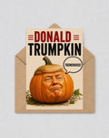 May include: A greeting card depicting a pumpkin with a face resembling Donald Trump, with a blonde hair-like top. The card reads "DONALD TRUMPKIN" in bold letters, with a speech bubble saying "TREMENDOUS!" The card is inside a brown envelope.